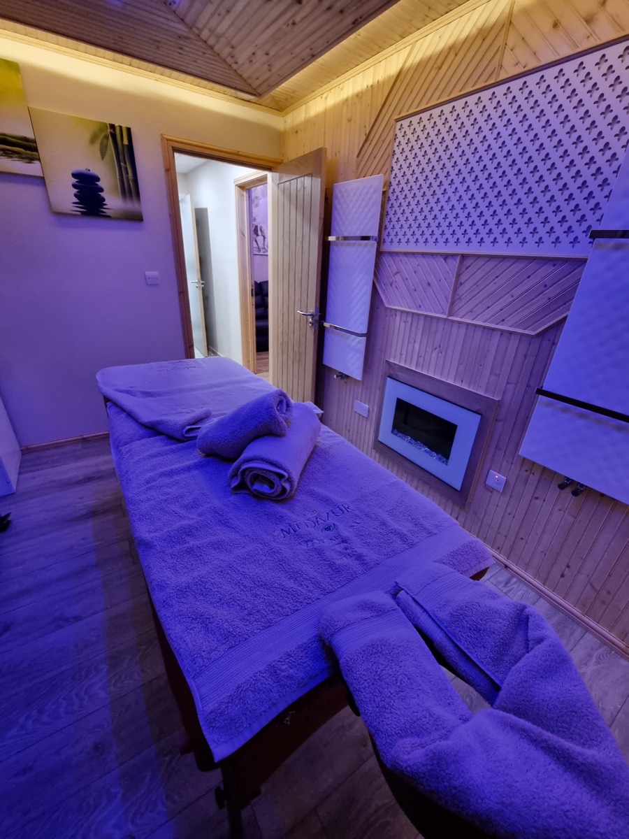 The Pressure London Massage treatment room with warm wooden panelling, a fireplace and soft lighting