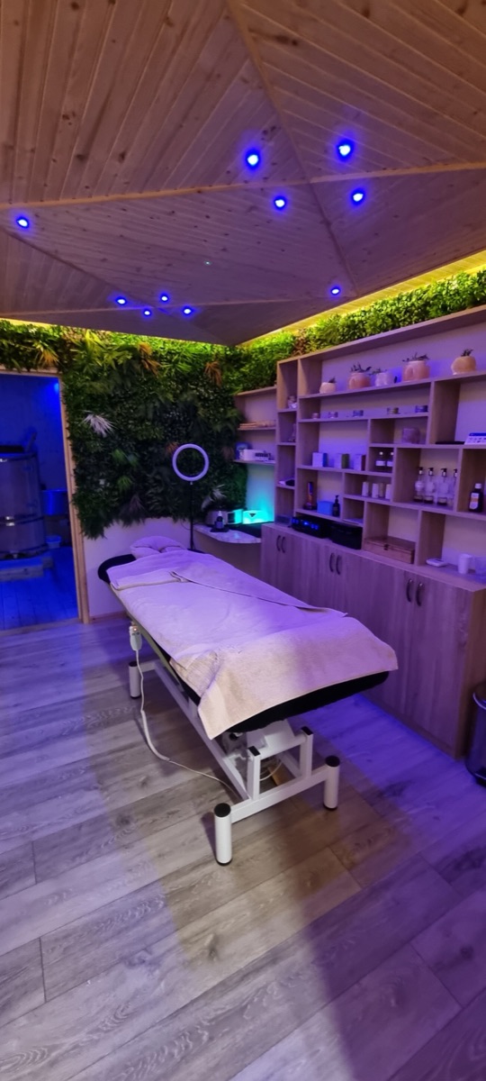Treatment room with a living green wall, massage couch and shelves of oils and salts