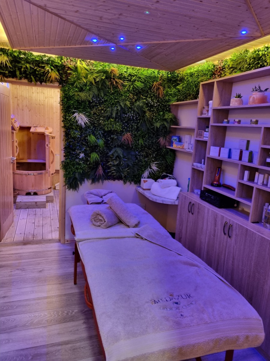 Treatment couch beside the green wall with a wooden sauna tub in the background